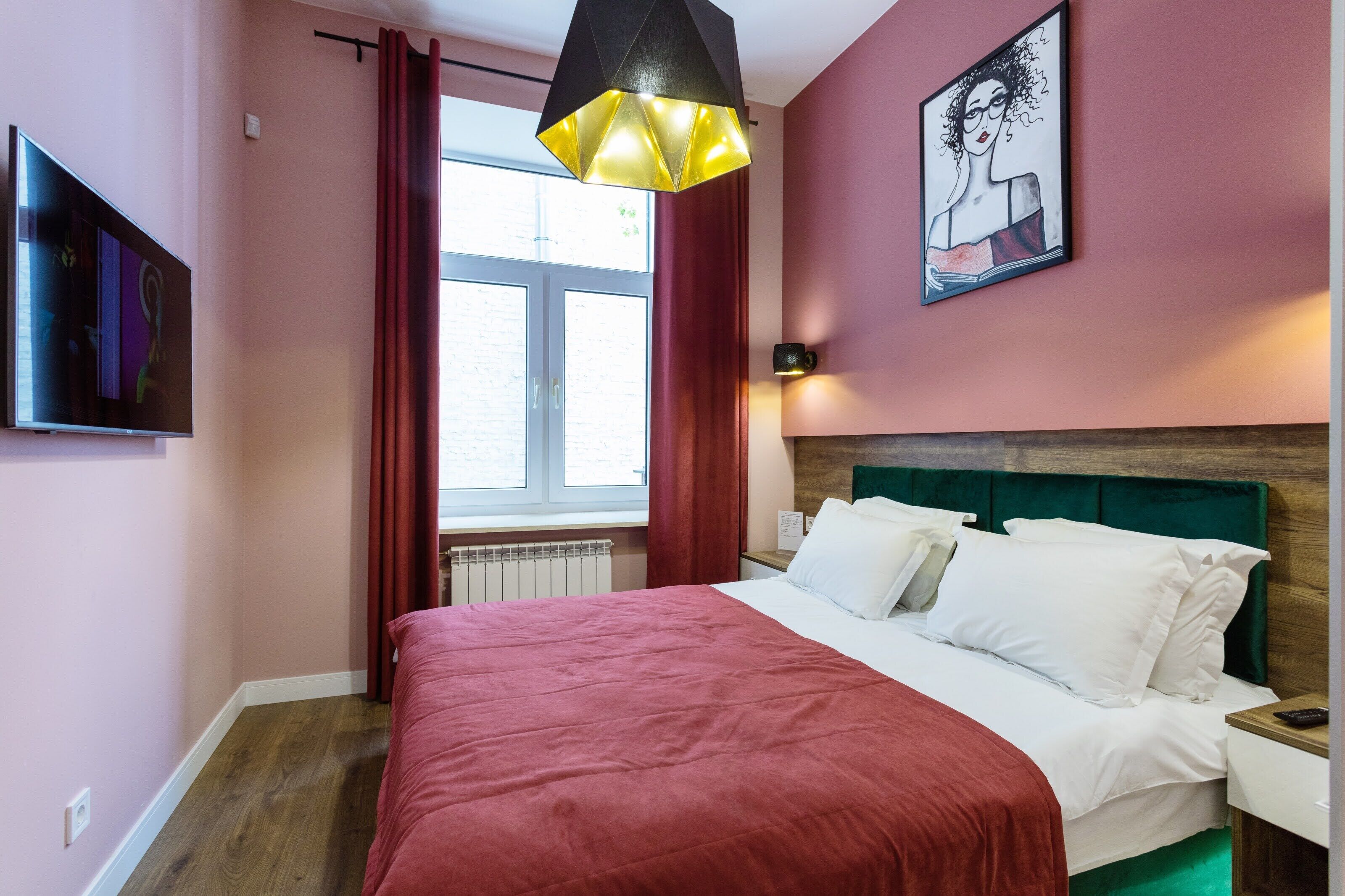 A bedroom with a bed, a window with red curtains, a painting on the wall, and a television on the left.