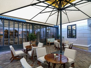 An outdoor seating area with tables and chairs, a large umbrella, and a view of the interior through glass doors.