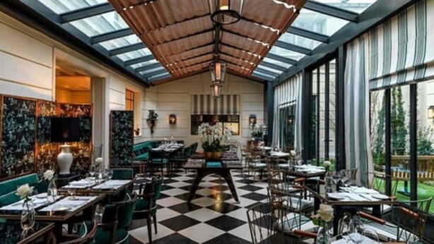 Un restaurant doté d’un sol à carreaux, de hauts plafonds avec un décor de lambris en bois et de grandes fenêtres offrant une vue sur l’extérieur.