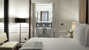 Une chambre d’hôtel avec un grand lit, une table de chevet, une lampe et une vue sur la salle de bain par une porte ouverte.