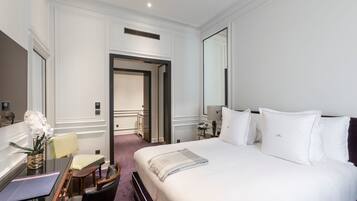 Ein Hotelzimmer mit einem großen Bett, einem Schreibtisch mit Stuhl, einem kleinen Tisch und einer Blumenvase.