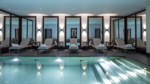 Une piscine intérieure moderne, dotée de chaises longues et de miroirs.