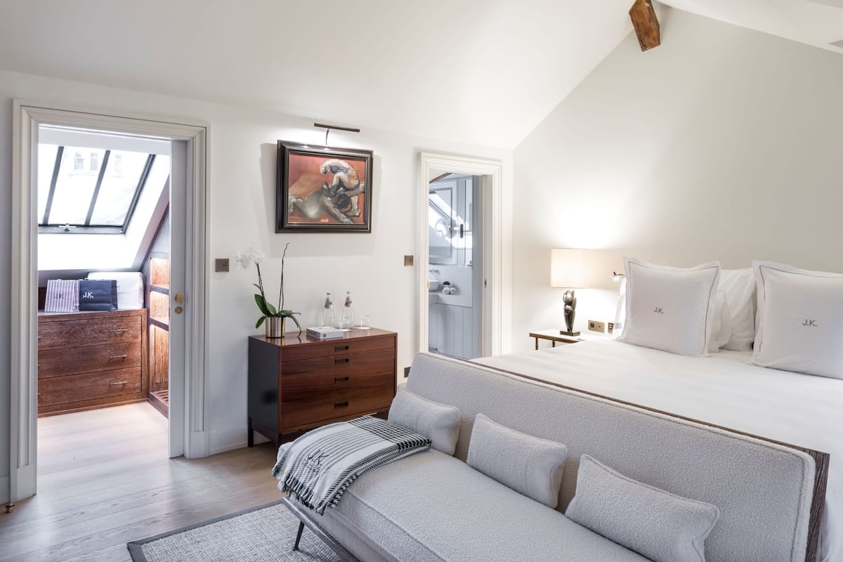 A modern bedroom with a large bed, a wooden dresser, a painting, and a skylight.