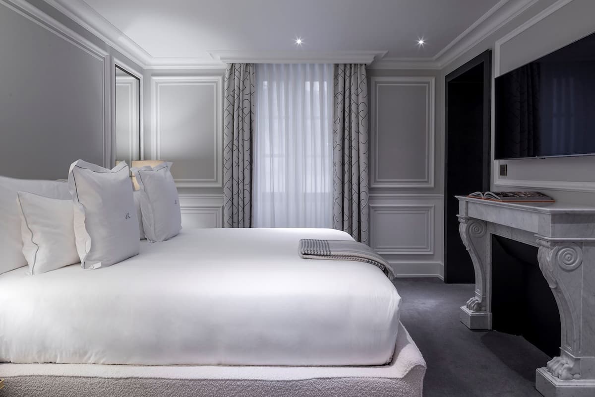A neatly arranged bedroom with a large bed, a bedside table, a mirror, and a television.