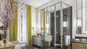 Une salle de bain moderne dotée d’une douche à parois de verre, d’un meuble-lavabo avec miroir et d’un coin salon avec une table et des chaises.