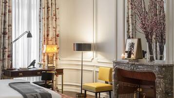 A hotel room with a bed, a desk with a lamp, a chair, a fireplace, and a mirror.