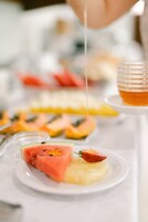 Una bandeja de postres con diversas frutas y un cucharón de miel.