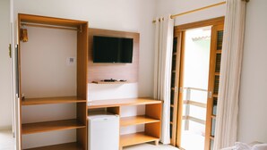 A room with a bed, a small white refrigerator, a wooden wardrobe, a mounted TV, and a sliding glass door with curtains. - Hotel Kiribati (São Sebastião)