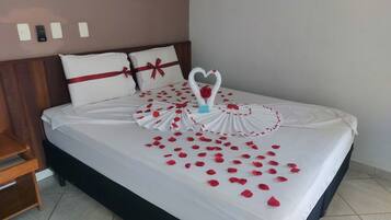 A neatly made bed with a white bedspread, red rose petals, and a heart-shaped decoration made of roses.