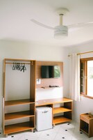 A compact room with a ceiling fan, a TV mounted on the wall, a small refrigerator, and a wooden shelf unit.