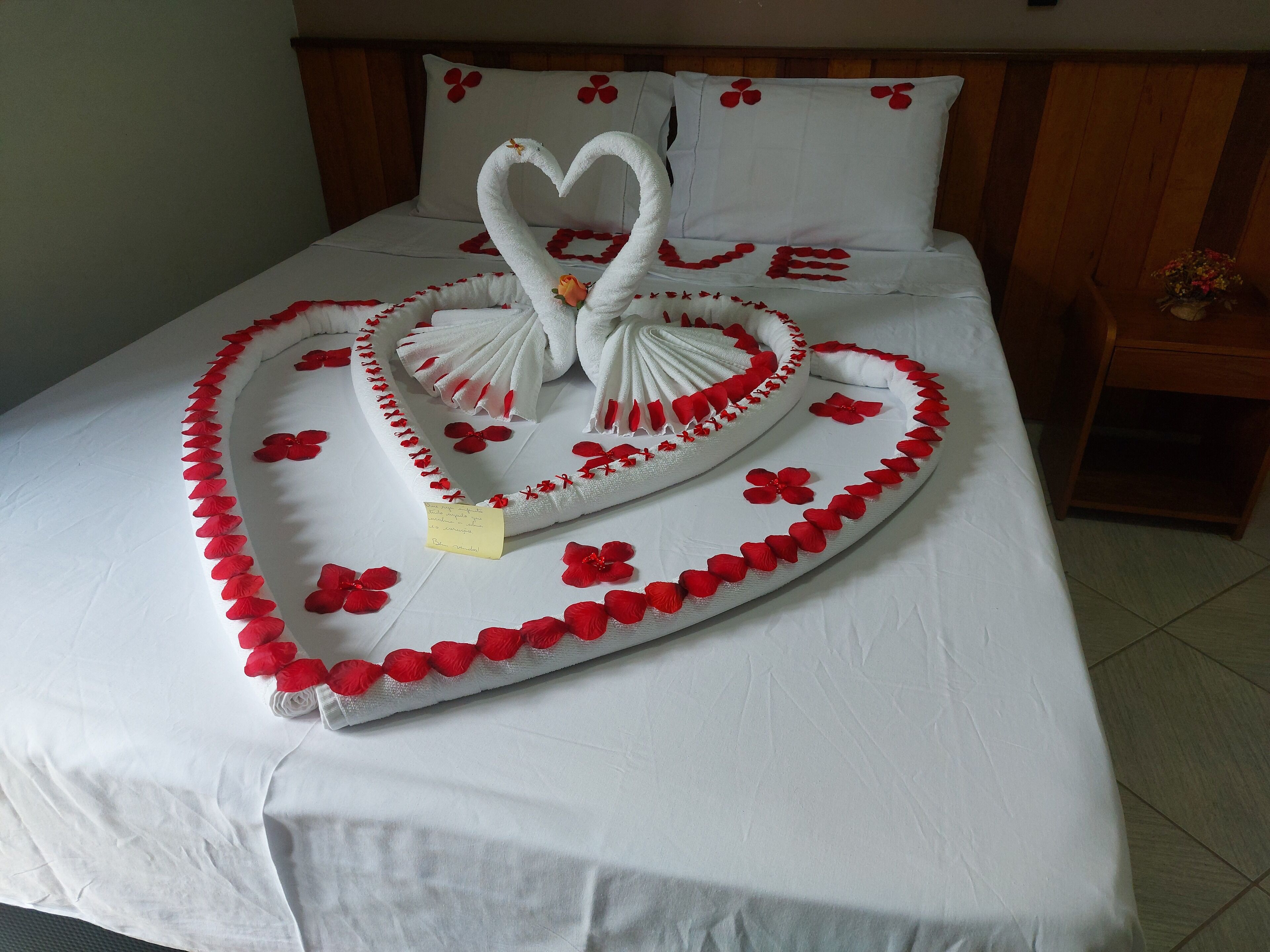 A bed with a heart-shaped towel arrangement featuring swans and red flowers.