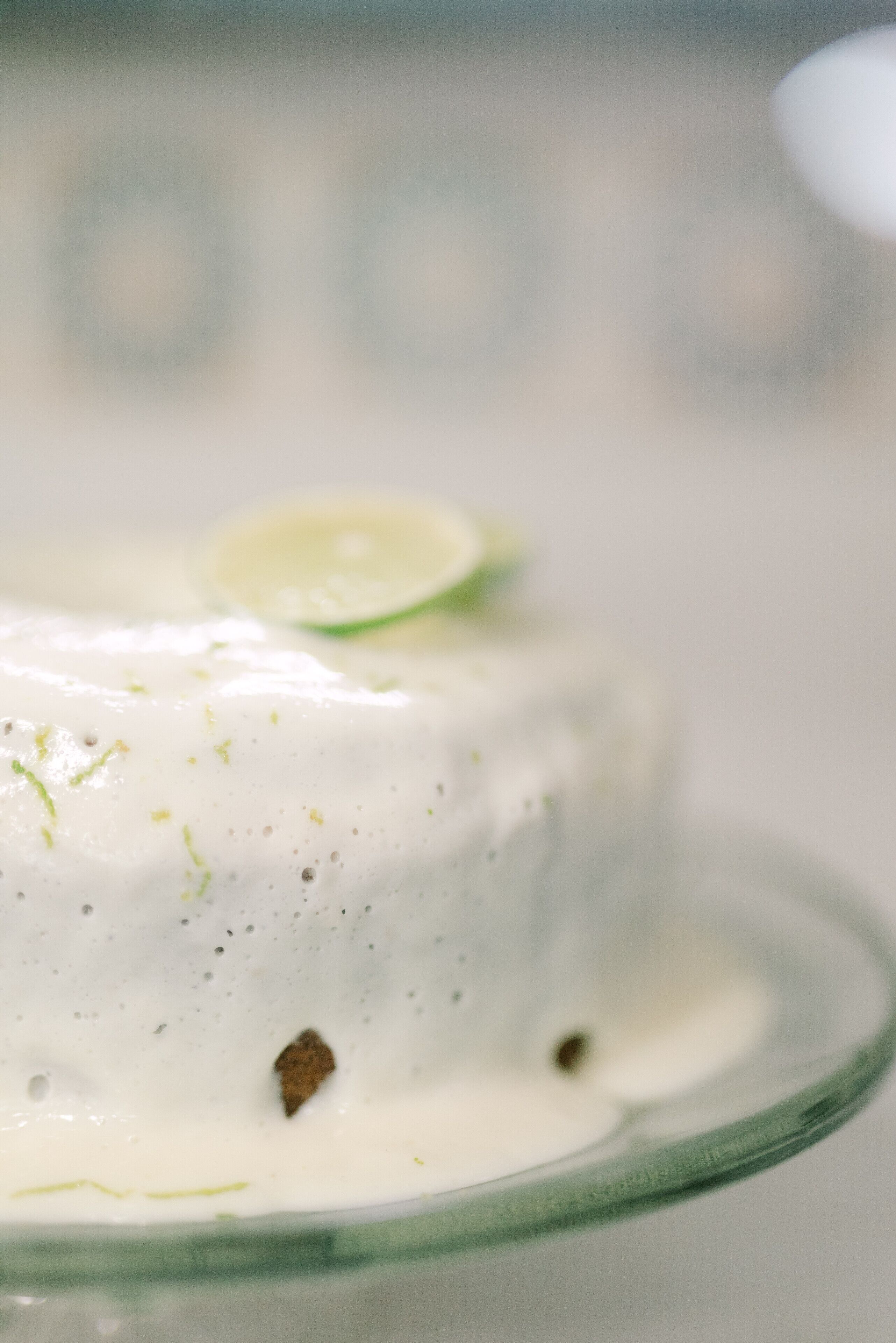 Une vue rapprochée d’un dessert à la texture crémeuse, garni d’une tranche de citron vert et de petites touches de couleur, servi sur une assiette en verre transparent.