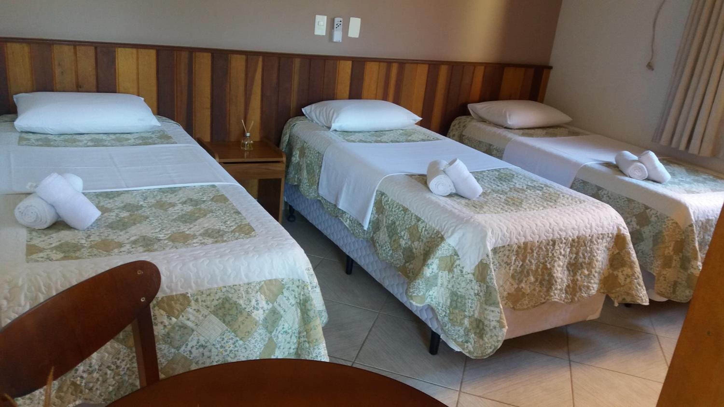 A hotel room with three single beds, each with a pillow and rolled towels.