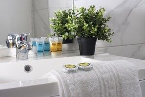 Um banheiro com pia branca, espelho, planta em vaso e artigos de higiene no balcão.
