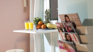 Une table de petit-déjeuner avec un panier de fruits, deux verres de jus d’orange et un présentoir à magazines contenant des numéros du magazine « ELLE ».