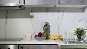 Une cuisine dotée d’une hotte en acier inoxydable, d’un pare-feu en marbre, d’un saladier rempli de fruits, d’une plante en pot et d’un évier.