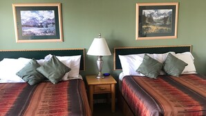 Camera d'albergo con due letti, ciascuno con testiera, comodino con lampada e quadri appesi alle pareti.