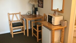 Una stanza piccola e funzionale con una scrivania in legno, due sedie, un piccolo frigorifero, un forno a microonde, una lampada, un telefono e un quadro appeso al muro.
