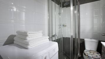 Ein modernes Badezimmer mit einer gläsernen Duschkabine, einer weißen Waschmaschine und einem WC mit Sitzbank aus Steinmosaik.