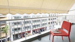 Un balcon avec une chaise rouge, une rambarde en métal et une vue sur un train et des bâtiments situés en contrebas.