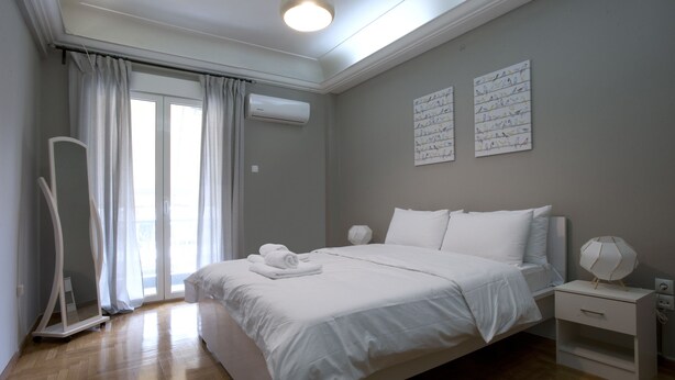Une chambre moderne avec un grand lit, une table de chevet, une commode et un climatiseur fixé au mur.