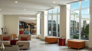 A spacious living area with modern furniture, large windows offering views of the outdoors, and a well-lit interior. - Hilton Garden Inn Olive Branch, MS (Olive Branch)
