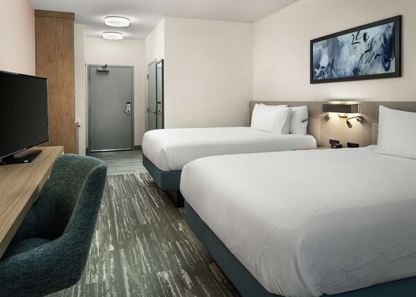 A hotel room with two beds, a desk with a flat-screen TV, a seating area, and a painting on the wall.