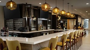 A bar area with a long counter, multiple bar stools, and hanging pendant lights. - Hilton Garden Inn Olive Branch, MS (Olive Branch)