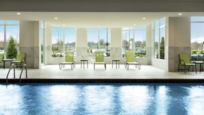A pool area with chairs and tables, large windows, and a view of the parking lot. - Hilton Garden Inn Olive Branch, MS (Olive Branch)
