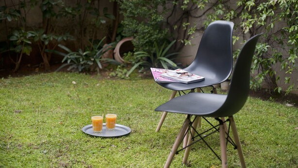 A modern outdoor seating area with a black chair and a table, a tray with two glasses of orange juice, and lush greenery in the background. - Cozy Fully Renovated Studio in Holargos (Papagou-Holargos)