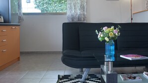 A modern living room with a black sofa, a glass coffee table, and a blue vase with flowers. - Cozy Fully Renovated Studio in Holargos (Papagou-Holargos)