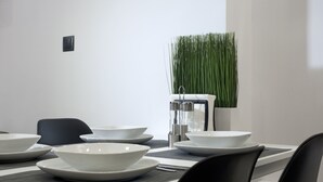 A modern dining area with a table set for four, including white plates and bowls, a water dispenser, and a potted plant. - Α Koukaki, Modern Newly Refurbished Apartment (Athens)