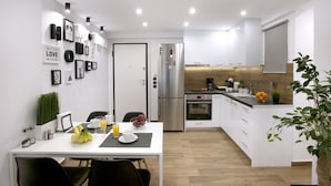 A modern kitchen with white cabinets, a stainless steel refrigerator, and a dining area with a white table and chairs. - Α Koukaki, Modern Newly Refurbished Apartment (Athens)