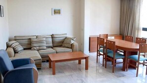 A living room with a sofa, a wooden coffee table, and a dining table with chairs. - Paraiso Florida (Benidorm)