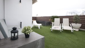 Une terrasse sur le toit, avec un revêtement d’herbe artificielle, des fauteuils blancs, une petite table et une plante en pot.