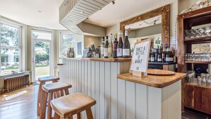 A bar area with wooden stools, a wine selection display, and a mirror above the bar. - St George's Hotel (Perranporth)