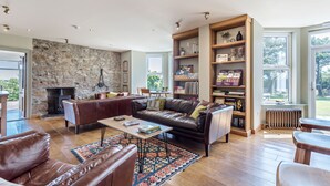 A spacious living room with a stone wall, leather sofas, a coffee table, and a bookshelf. - St George's Hotel (Perranporth)