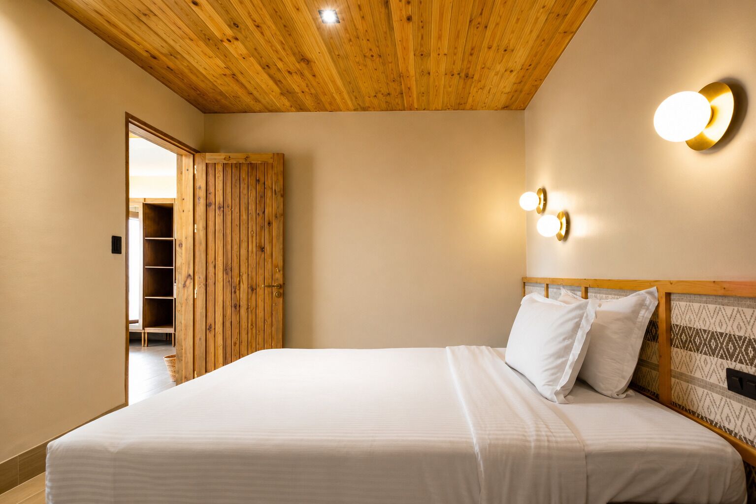 Een slaapkamer met een houten plafond, een bed met wit beddengoed, een houten garderobe en wandlampen.