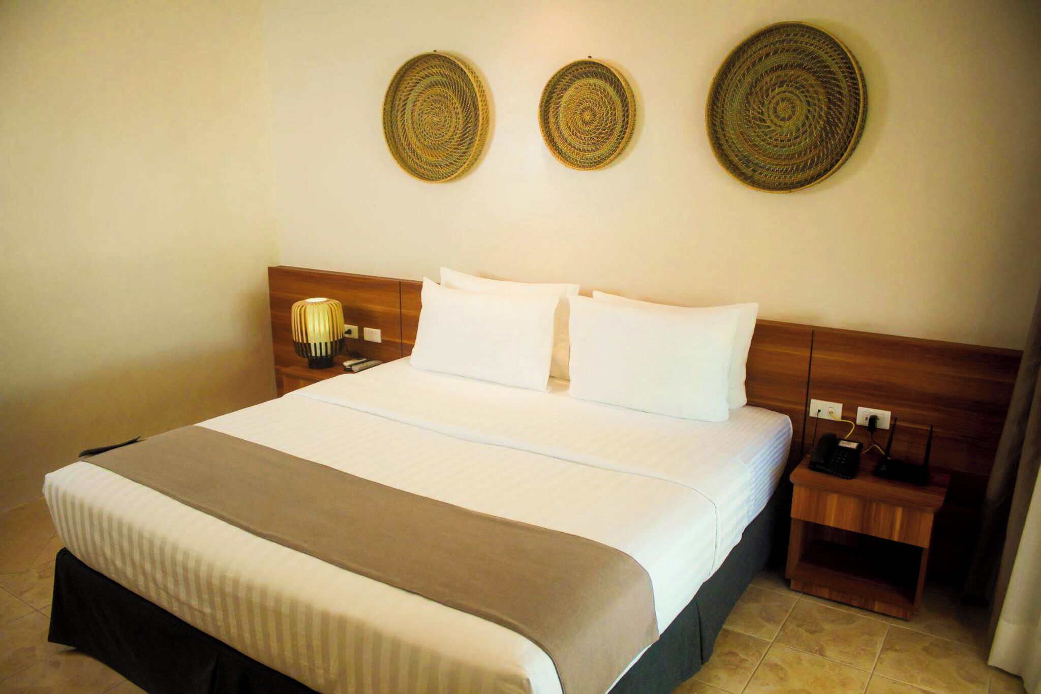 A hotel room with a large bed, a wooden headboard, two bedside tables, and decorative woven wall hangings.