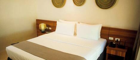A hotel room with a large bed, a wooden headboard, two bedside tables, and decorative woven wall hangings.