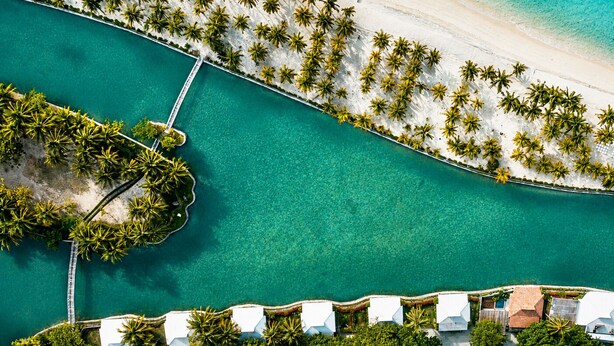 An aerial view of a resort with a beach, clear turquoise waters, and a row of white buildings with a dock. - Golden Sands Destination Resorts (Daanbantayan)