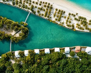 An aerial view of a resort with a beach, clear turquoise waters, and a row of white buildings with a dock. - Golden Sands Destination Resorts (Daanbantayan)