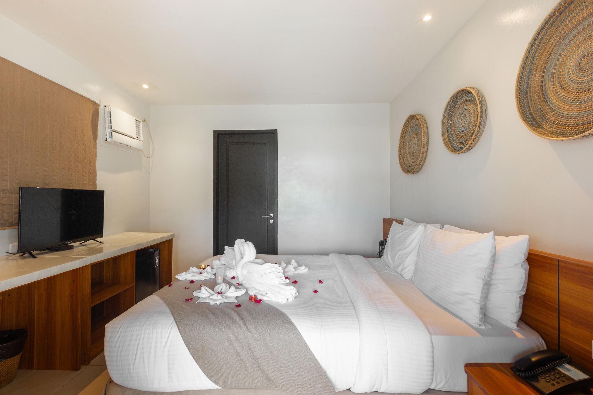 Una habitación de hotel con una cama, un escritorio con televisor, una puerta y decoración en la pared.