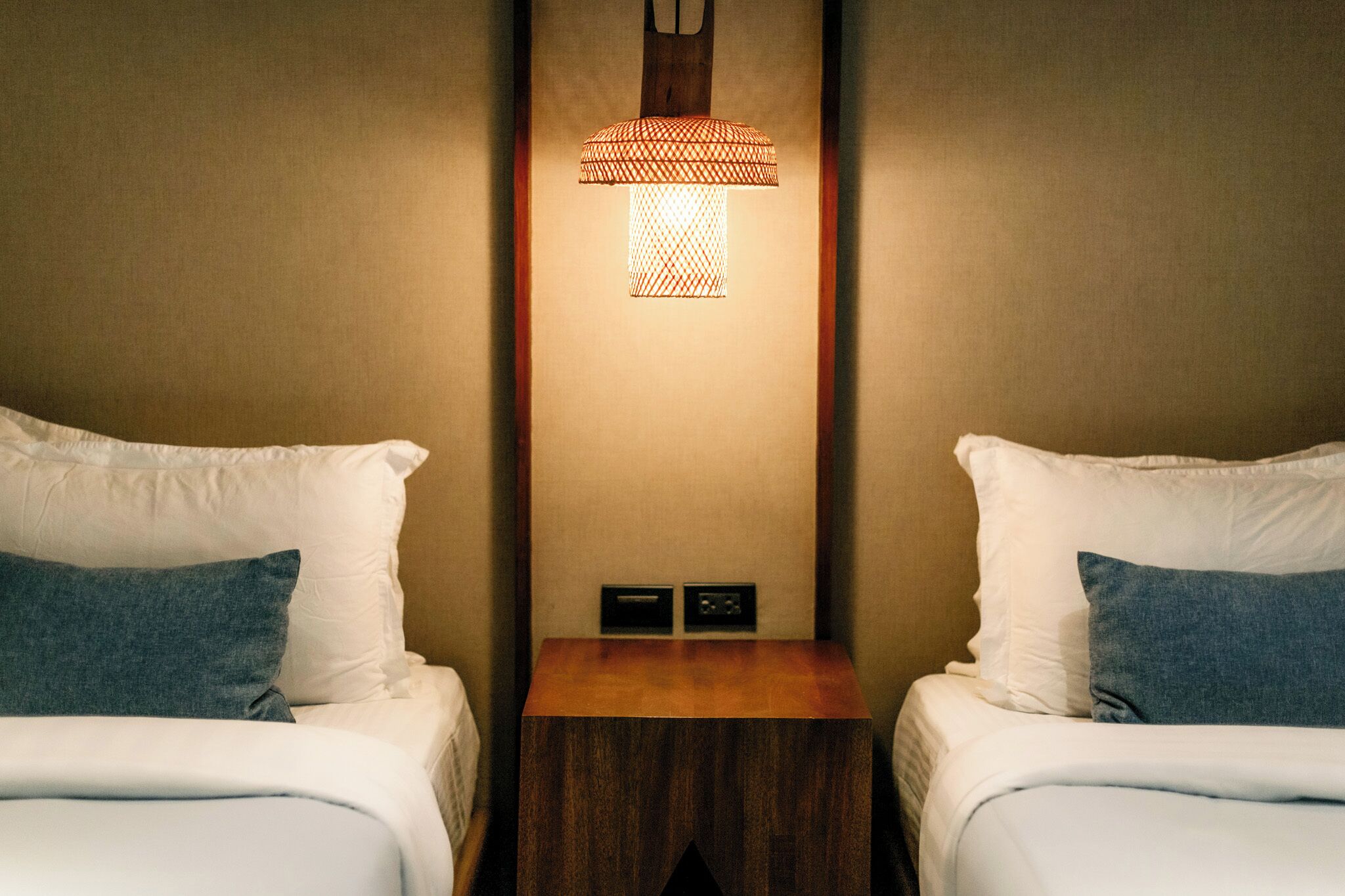 Habitación de hotel con dos camas, una mesita de noche, una lámpara de pared y un panel de control.