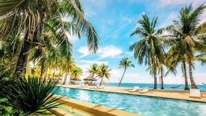 A pool area with lounge chairs, palm trees, and a view of the ocean. - Golden Sands Destination Resorts (Daanbantayan)