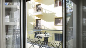 A balcony with a table and chairs, a small table with a plant, and a window with blinds. - Victoria Square, Cozy and Stylish Apartment (Athens)
