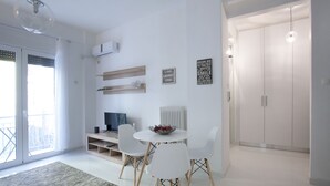 A modern living room with a white dining table, four white chairs, a glass ceiling light, a white radiator, and a white wardrobe. - Victoria Square, Cozy and Stylish Apartment (Athens)