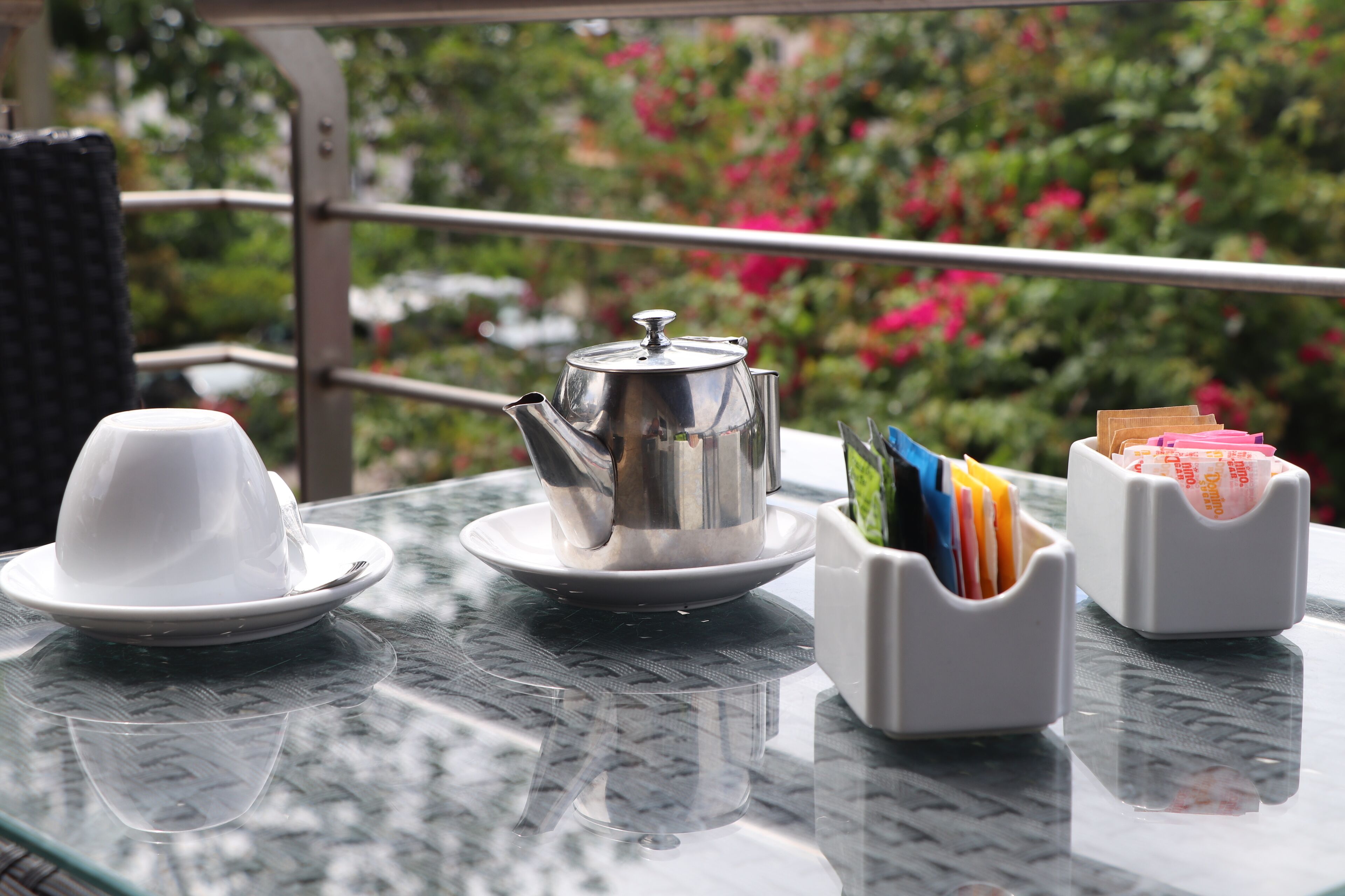 Una mesa con tetera, tazas y un atril de tarjetas, al aire libre con vista a un jardín.