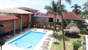 Una piscina con sillas de descanso, una estructura de techo de paja y palmeras.