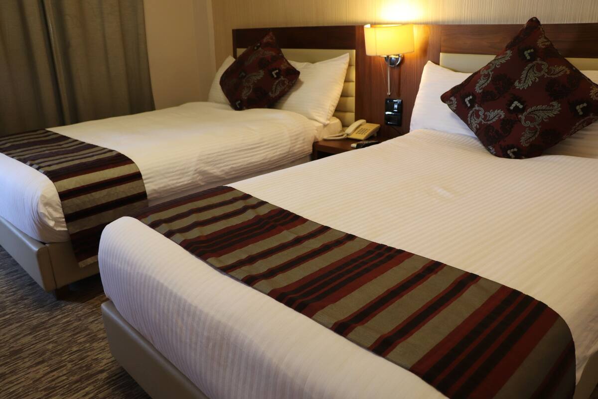 Two adjacent hotel beds with striped bedspreads, a bedside telephone, and a lamp on the nightstand.